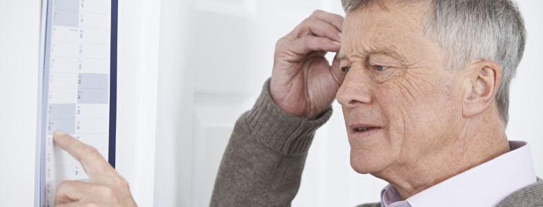 Confused Senior Man With Dementia Looking At Wall Calendar